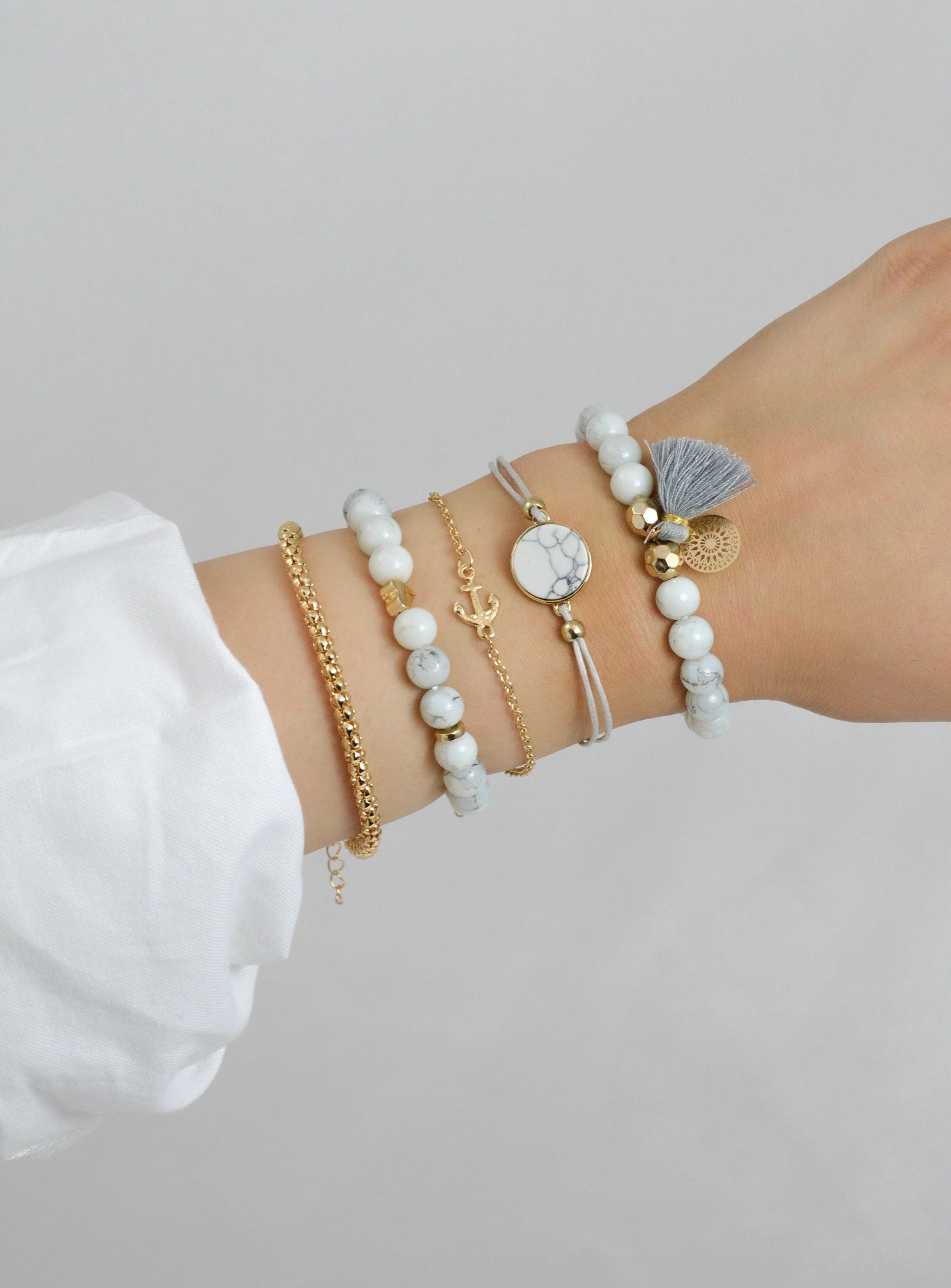 5‑teiliges Armband Set Didyma getragen am Handgelenk – weiß, grau und goldfarben Modeschmuck