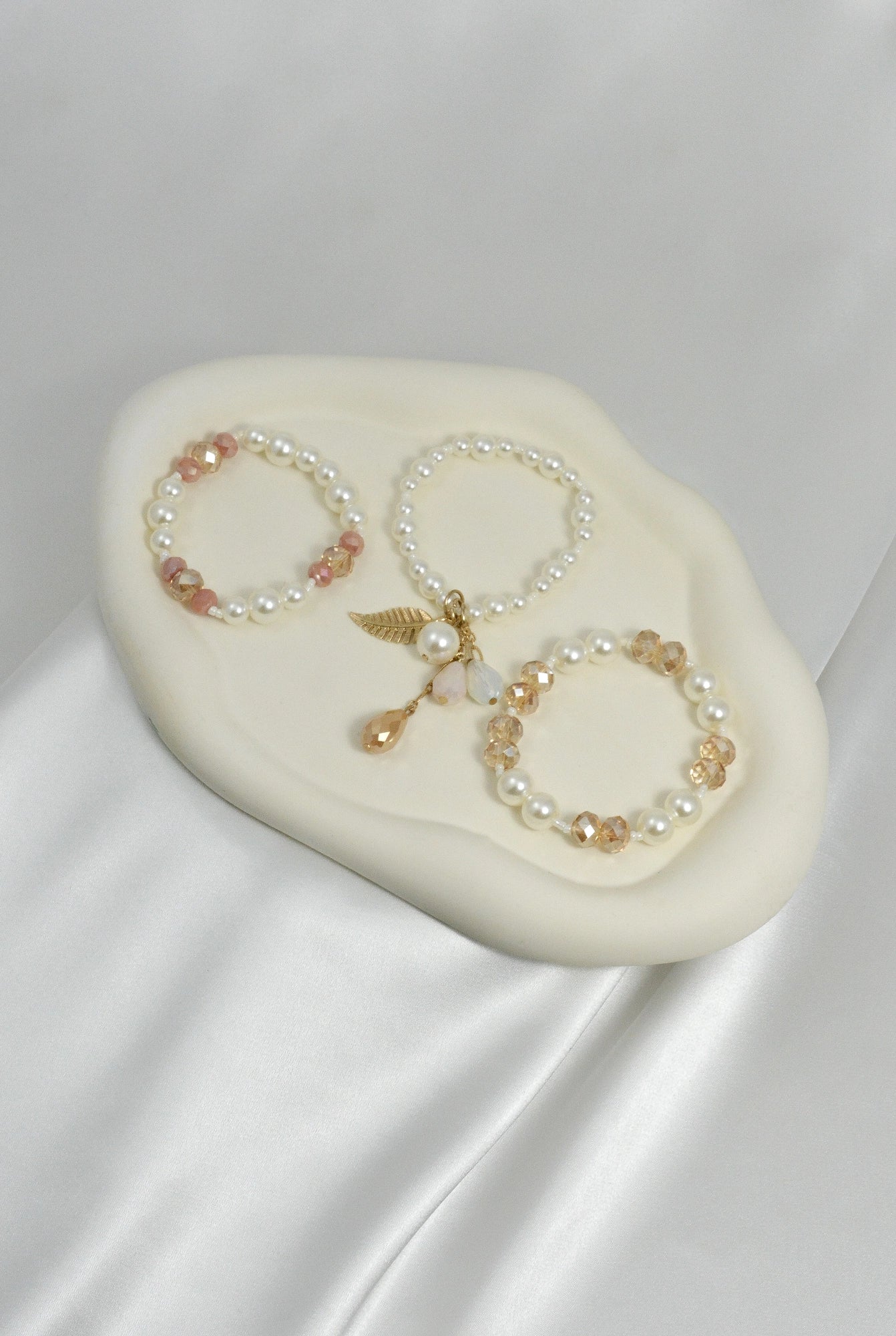 Goldy Feather Armband Set liegend – einzelne weiße, rosa und goldfarbene Armbänder mit Feder‑Elementen